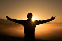 Silhouette of a man standing like Jesus on the Cross facing the sunset