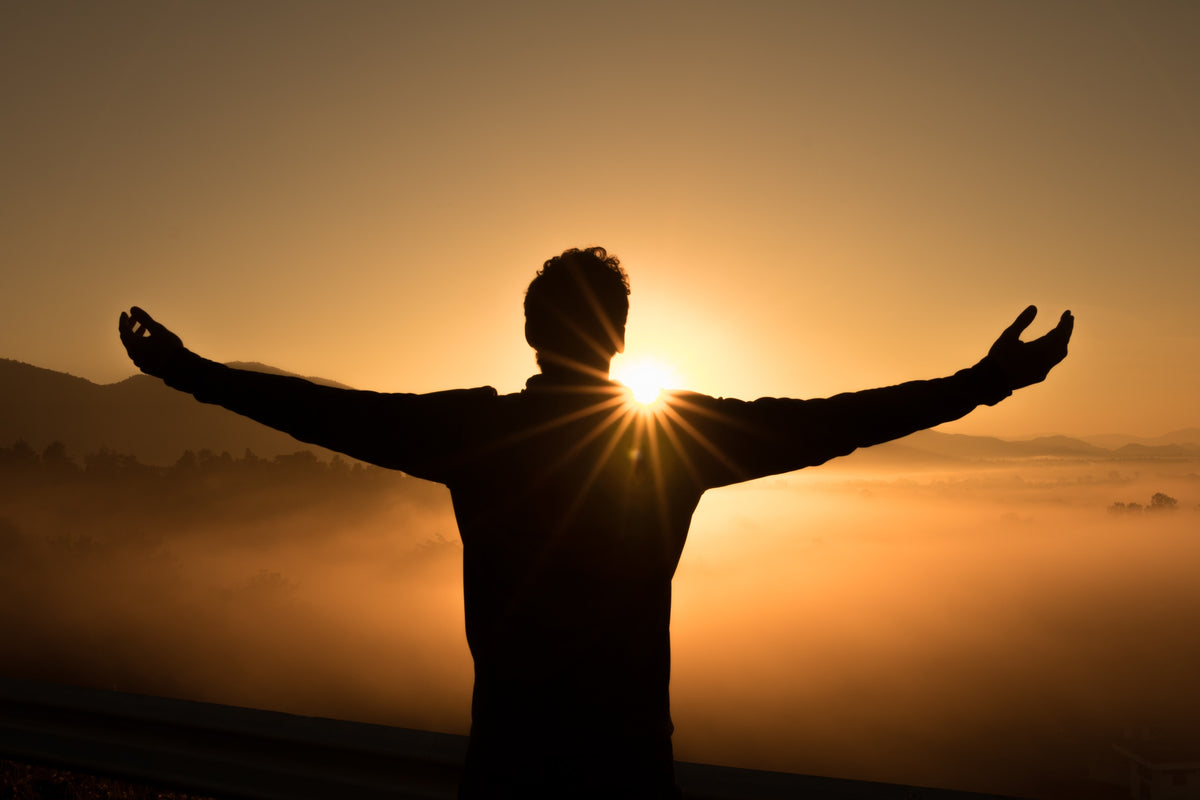Silhouette of a man standing like Jesus on the Cross facing the sunset